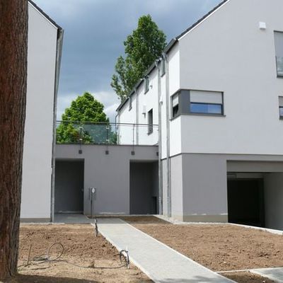 Im Mai 2013 ist die Wohnanlage des Architekten Peter Faust aus Mainz bezugsfertig. Die Wege zu den einzelnen Häusern führen unter den hohen Baumkronen der Kiefern durch die zukünftige Vorgartenbepflanzung.