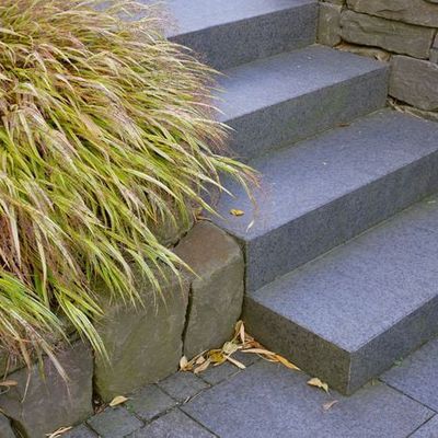 Mitte Oktober färbt sich Hakonechloa macra 'Aureola' pfirsichfarben ein. Das üppig herabhängende Gras passt hervorragend zu der Trockenmauer aus Bergischer Grauwacke.